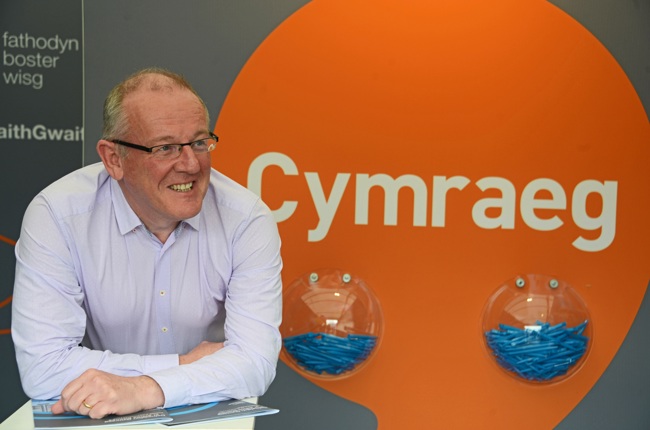 Aled Roberts in front of iaith gwaith logo